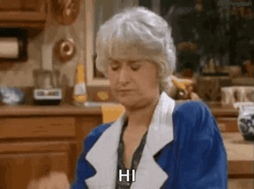 a woman in a blue jacket is sitting in a kitchen and says hi .