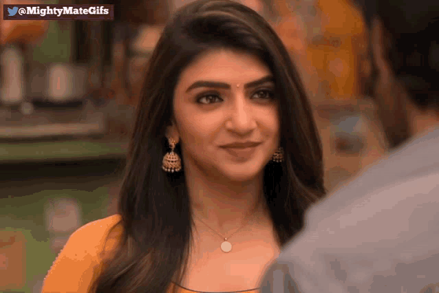 a woman wearing a necklace and earrings looks at a man with a mightymategifs watermark