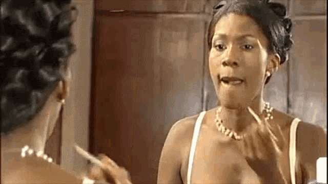 a woman is applying makeup in front of a mirror while wearing a pearl necklace .