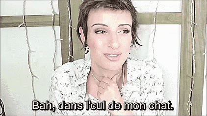 a woman with short hair is sitting in front of a window and talking in french .