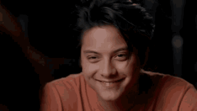 a young man is smiling and looking at the camera while wearing an orange shirt .