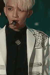 a man with a microphone in his mouth is wearing a black shirt and white jacket .