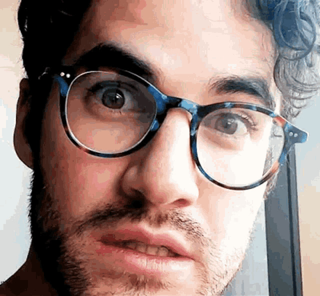 a close up of a man wearing glasses and making a face