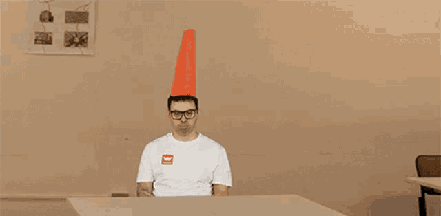 a man with a cone on his head points to the word burro on the wall behind him