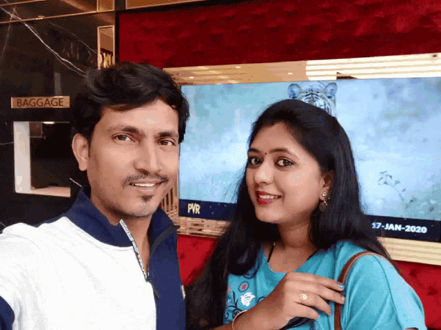 a man and a woman are posing for a picture in front of a tv screen that says baggage
