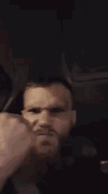 a man with a beard is making a funny face while sitting in a car at night .