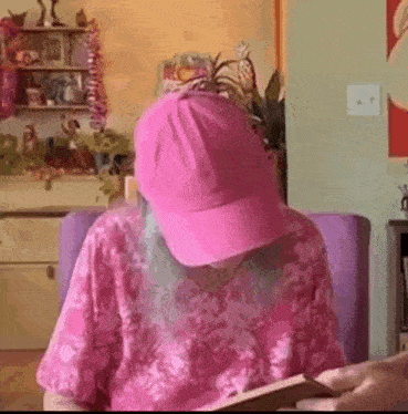 a woman with blue hair and a pink hat is sitting in a chair reading a book .