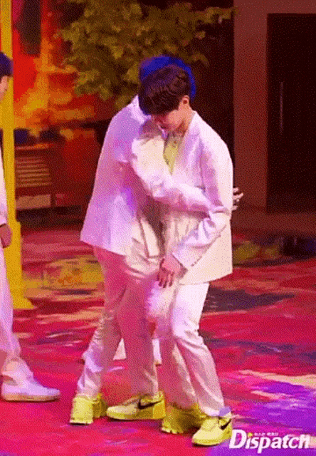 two men are hugging each other on a stage while wearing white clothes and yellow shoes .