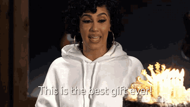 a woman in a white hoodie is holding a cake with candles on it and says this is the best gift ever