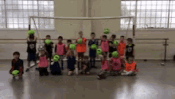 a group of children are posing for a picture in a gym with soccer balls