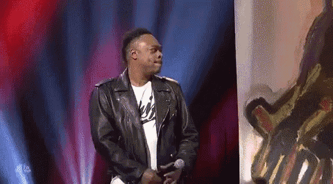 a man in a leather jacket is singing into a microphone on stage .
