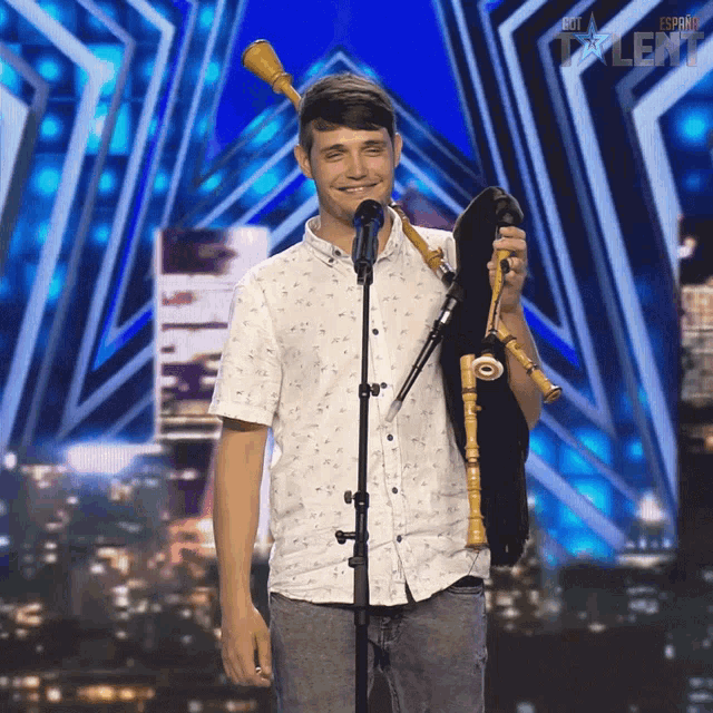 a young man stands in front of a microphone holding a bagpipe in front of a sign that says espana talent