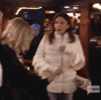 a woman in a white fur coat is talking to another woman with a bravo logo behind her