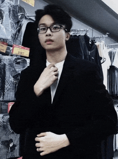 a young man wearing glasses and a black jacket is adjusting his tie