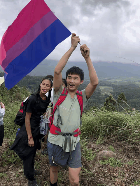 a man holds up a bisexual flag while standing on top of a hill