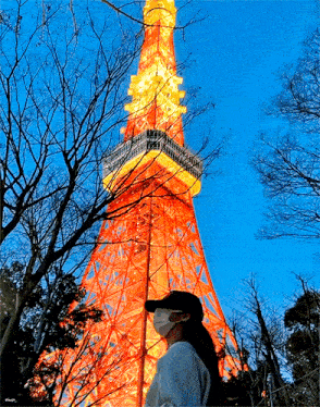 a woman wearing a mask stands in front of a very tall building