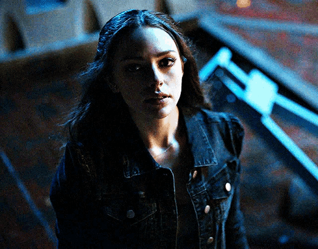 a woman wearing a black denim jacket stands in a dark room