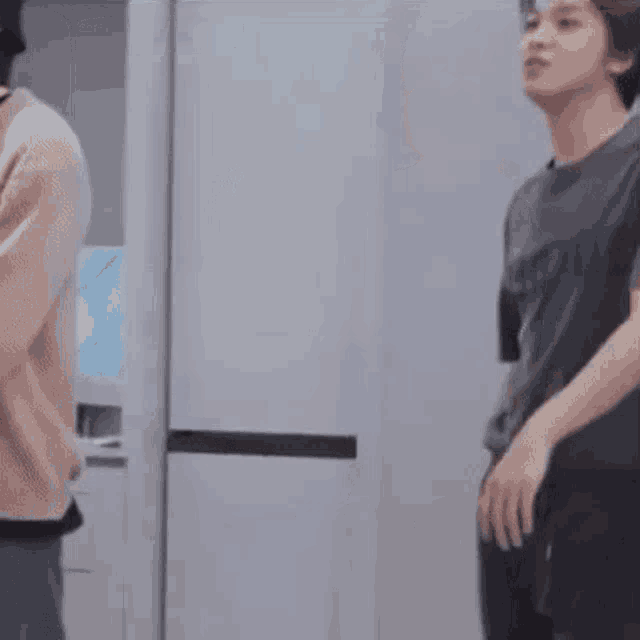 a young man in a gray shirt and black pants is standing in front of a refrigerator .