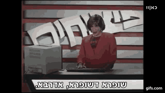 a woman in a red jacket is sitting at a desk in front of a computer and a sign that says 11