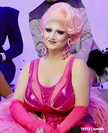 a drag queen in a pink dress and pink gloves is smiling .