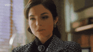 a woman with a brooch on her neck looks at the camera with the word voyo in the upper right corner