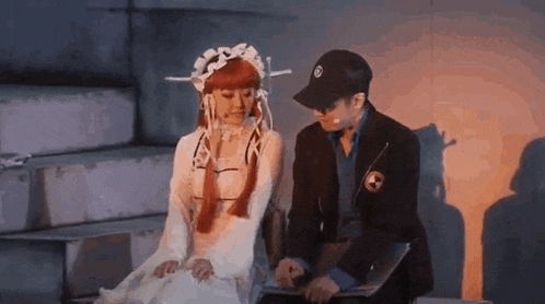 a man and a woman are sitting next to each other on a stage . the woman is wearing a white dress .