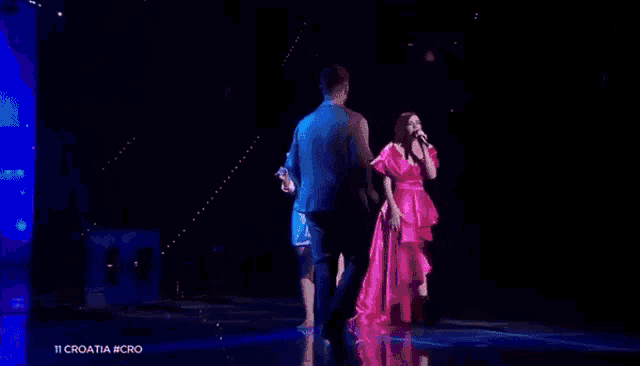 a woman in a pink dress is standing on a stage singing into a microphone .
