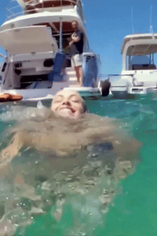 a man is swimming in the ocean while a man sits on a boat in the background
