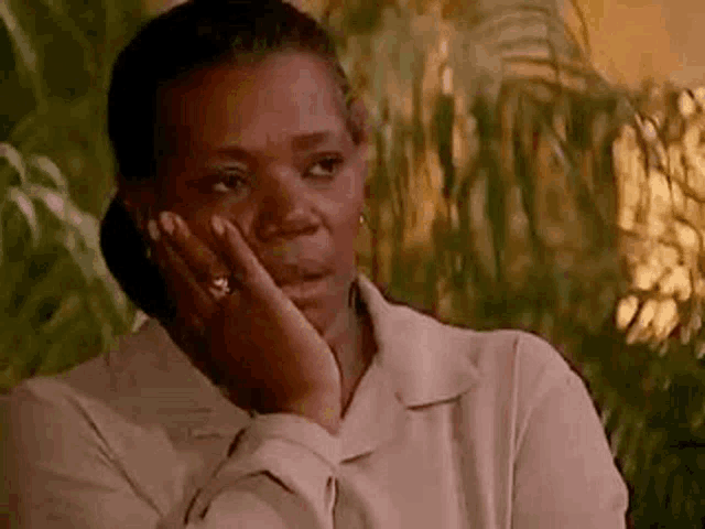 a woman is sitting in front of a palm tree and holding her hand to her face .