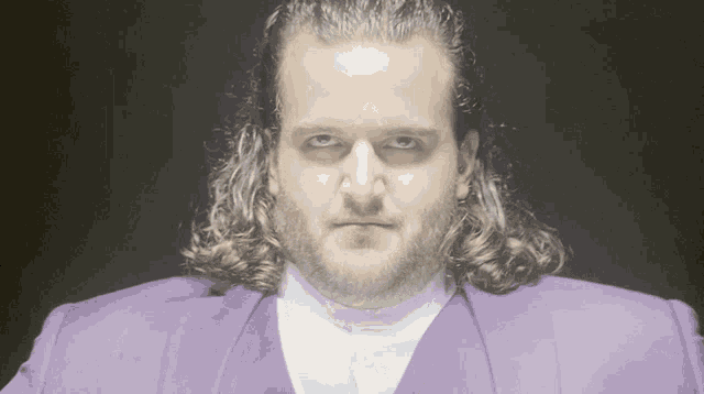 a man with long hair is wearing a purple suit