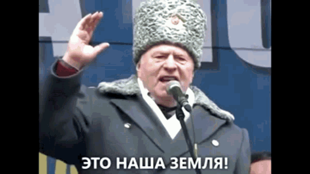 a man in a military uniform is speaking into a microphone with the words " это наша земля " below him