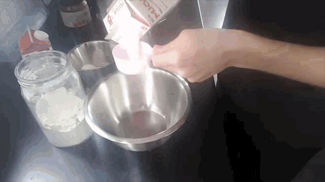 a person pouring milk into a metal bowl from a carton