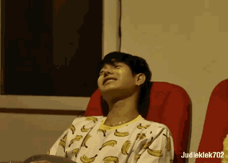a man wearing a shirt with bananas on it sits in a chair
