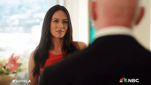 a woman in a red dress is looking at a bald man in a suit with the nbc logo on the bottom right