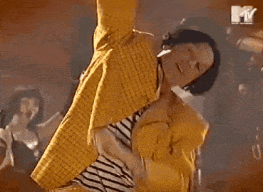 a woman in a yellow jacket is dancing in front of a mtv sign