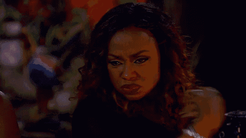 a woman is making a funny face while sitting at a table in a dark room .
