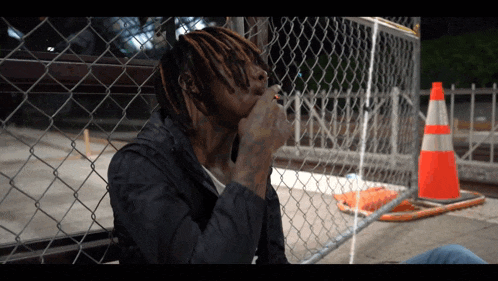 a man sitting in front of a chain link fence smoking