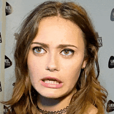 a woman is making a funny face in front of a wall that has uel written on it