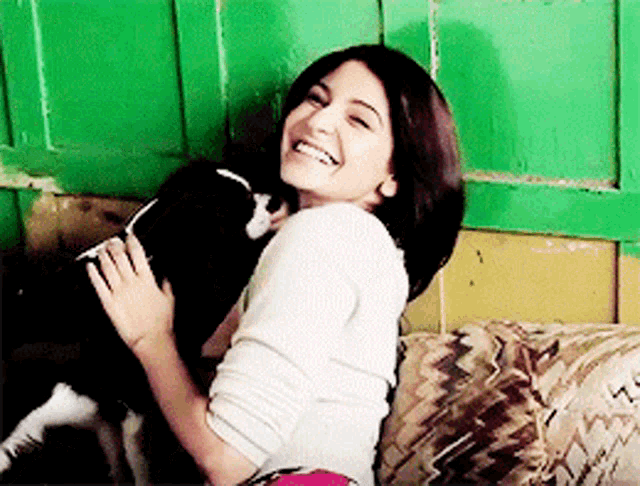 a woman is sitting on a couch holding a black and white dog