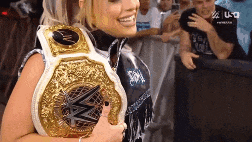 a woman is smiling while holding a wrestling championship belt .