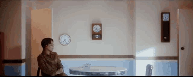 a man is sitting at a table with a clock on the wall above him