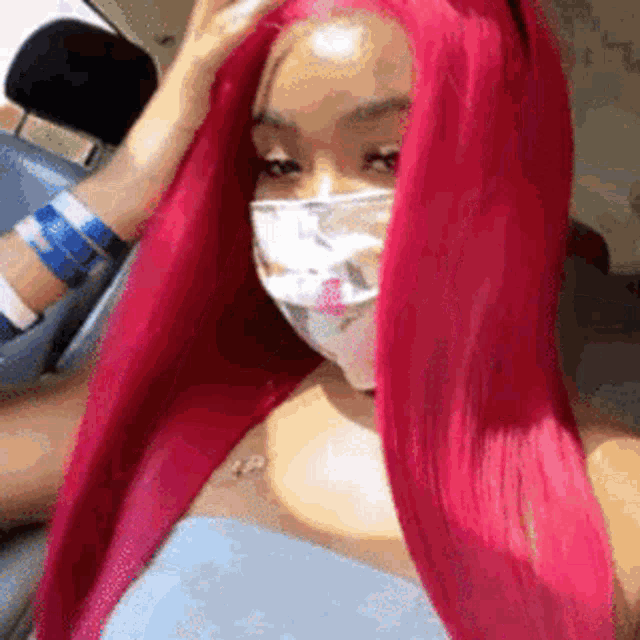 a woman with long pink hair is wearing a mask while sitting in a car .