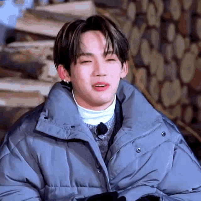 a young man wearing a gray jacket and a white turtleneck is smiling with his eyes closed .