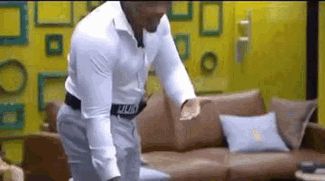 a man in a white shirt and gray pants is standing in front of a couch .
