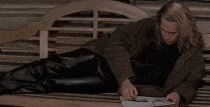 a man laying on a wooden bench reading a book