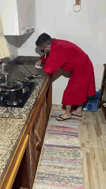a man in a red robe and flip flops is standing in a kitchen
