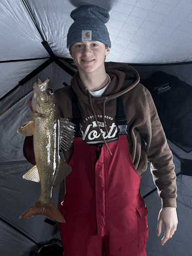 a young man holding a large fish wearing a shirt that says vert