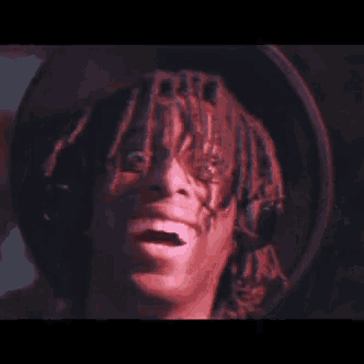a close up of a person 's face with dreadlocks and a hand on their head .