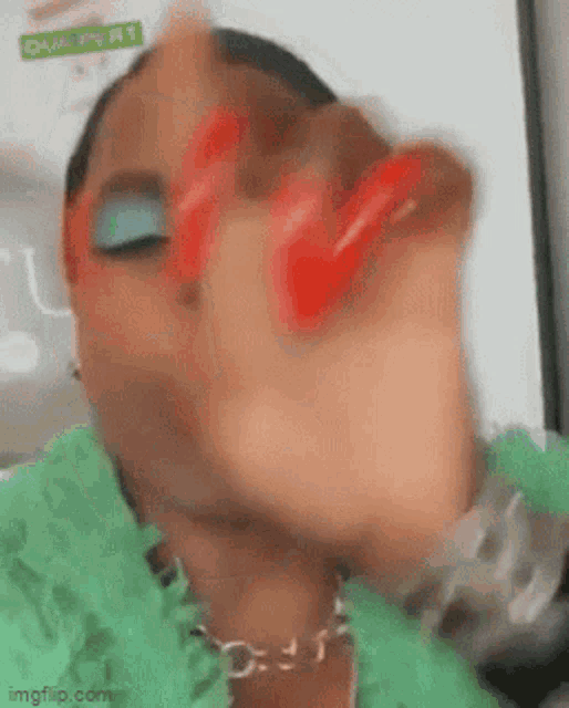 a woman wearing a green jacket and red nails is making a funny face .