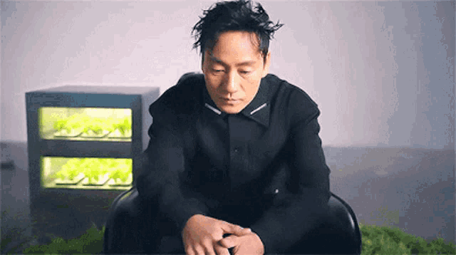 a man in a black shirt is sitting in a chair with his hands folded .